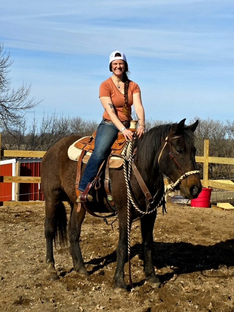 A young lady in a baseball cap riding a dark brown Morgan Mare in a corral.